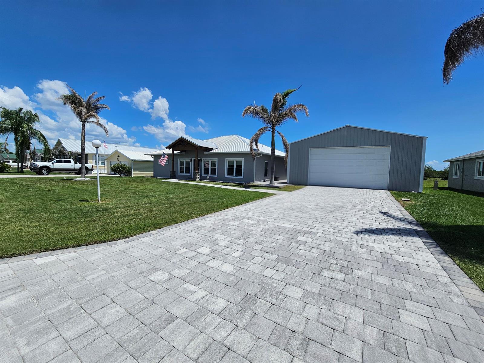 A gray house with a metal roof and a detached garage sits behind a paver driveway — 926 SW 44th Boulevard, Okeechobee FL 34974, OKEECHOBEE, FL