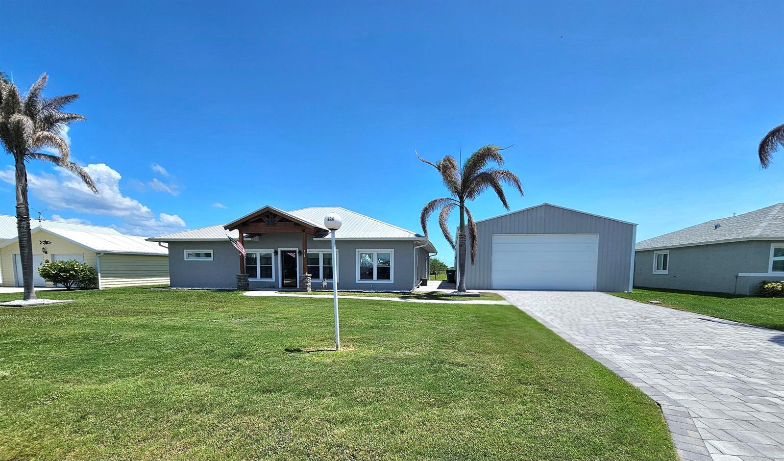 A gray single-story house with a detached garage and a paved driveway under a blue sky — 926 SW 44th Boulevard, Okeechobee FL 34974, OKEECHOBEE, FL