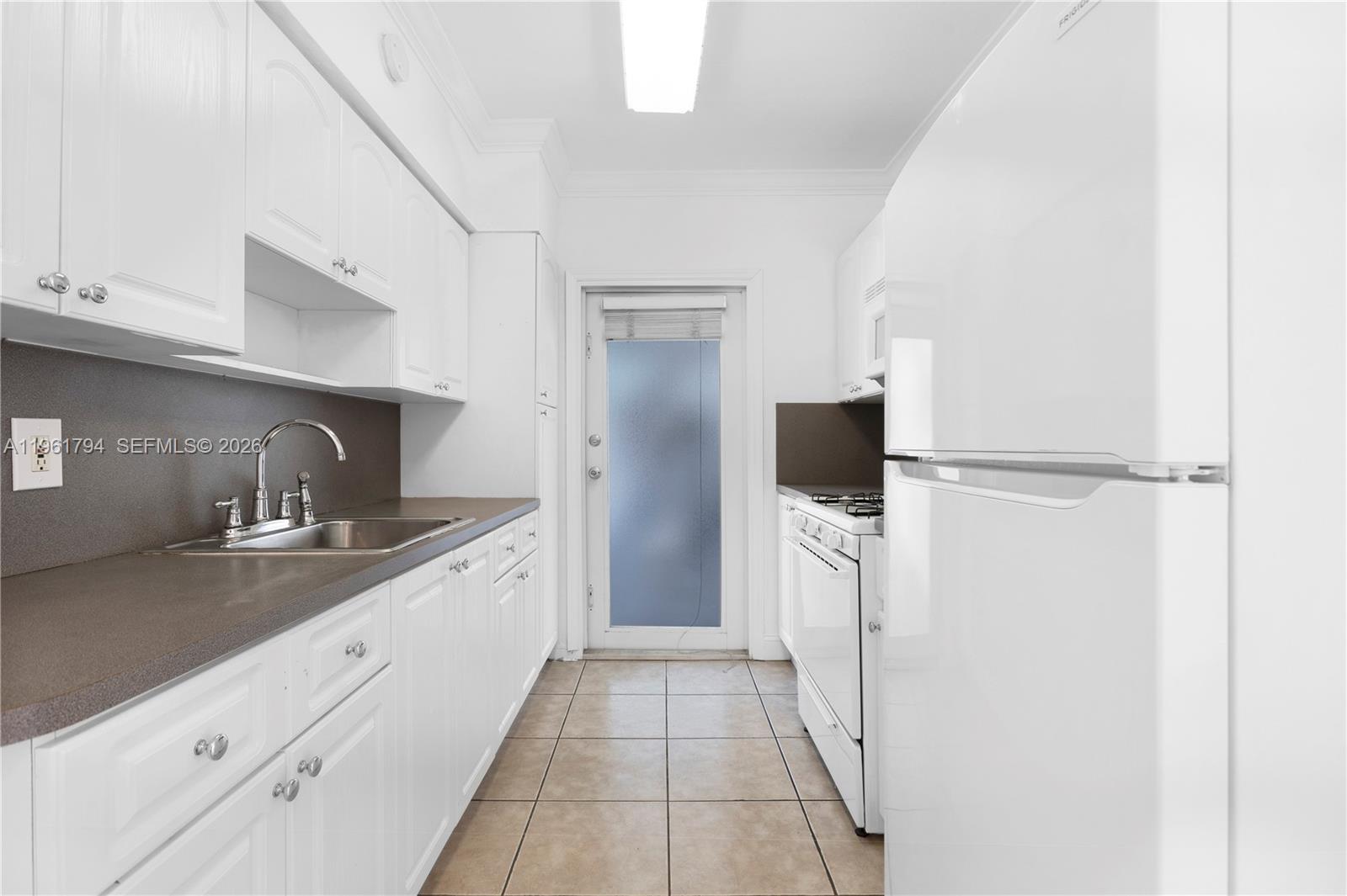 A galley-style kitchen features white cabinets, a dark countertop, and a glass-paneled exterior door — 315 69th St # 112, Miami Beach FL 33141, MIAMI BEACH, FL