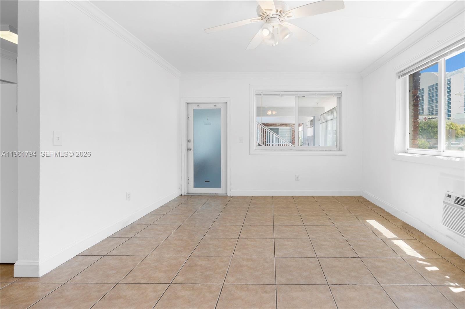 An empty room features white walls, tan tile flooring, a ceiling fan, and a glass door — 315 69th St # 112, Miami Beach FL 33141, MIAMI BEACH, FL
