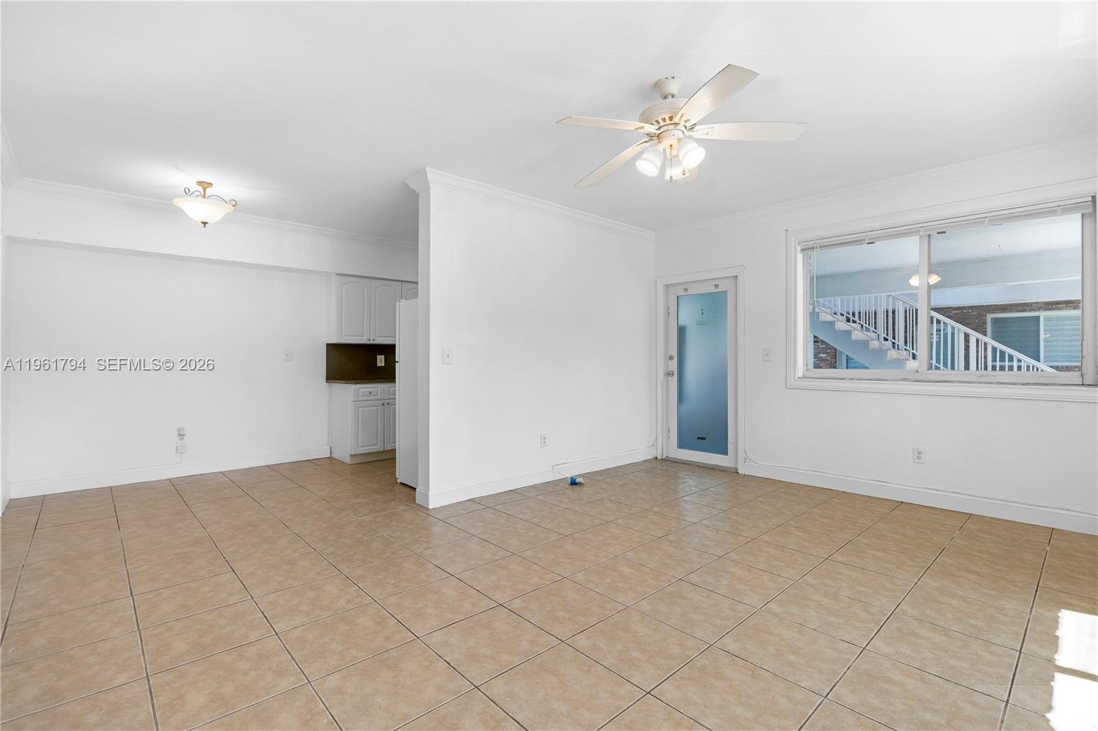An empty room features beige tile flooring, white walls, a ceiling fan, and a kitchen — 315 69th St # 112, Miami Beach FL 33141, MIAMI BEACH, FL