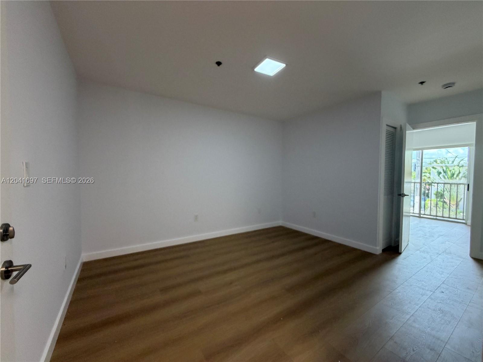An empty room features light-colored walls, wood-look flooring, a ceiling light, and a balcony doorway — 717 SW 11th Ave # 206, Miami FL 33130, MIAMI, FL