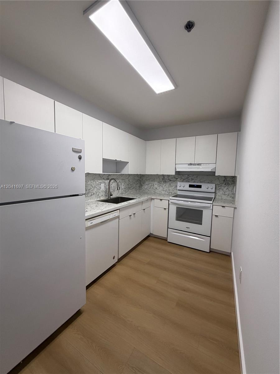 A galley kitchen features white cabinets, marble-look countertops, and light wood-tone flooring — 717 SW 11th Ave # 206, Miami FL 33130, MIAMI, FL