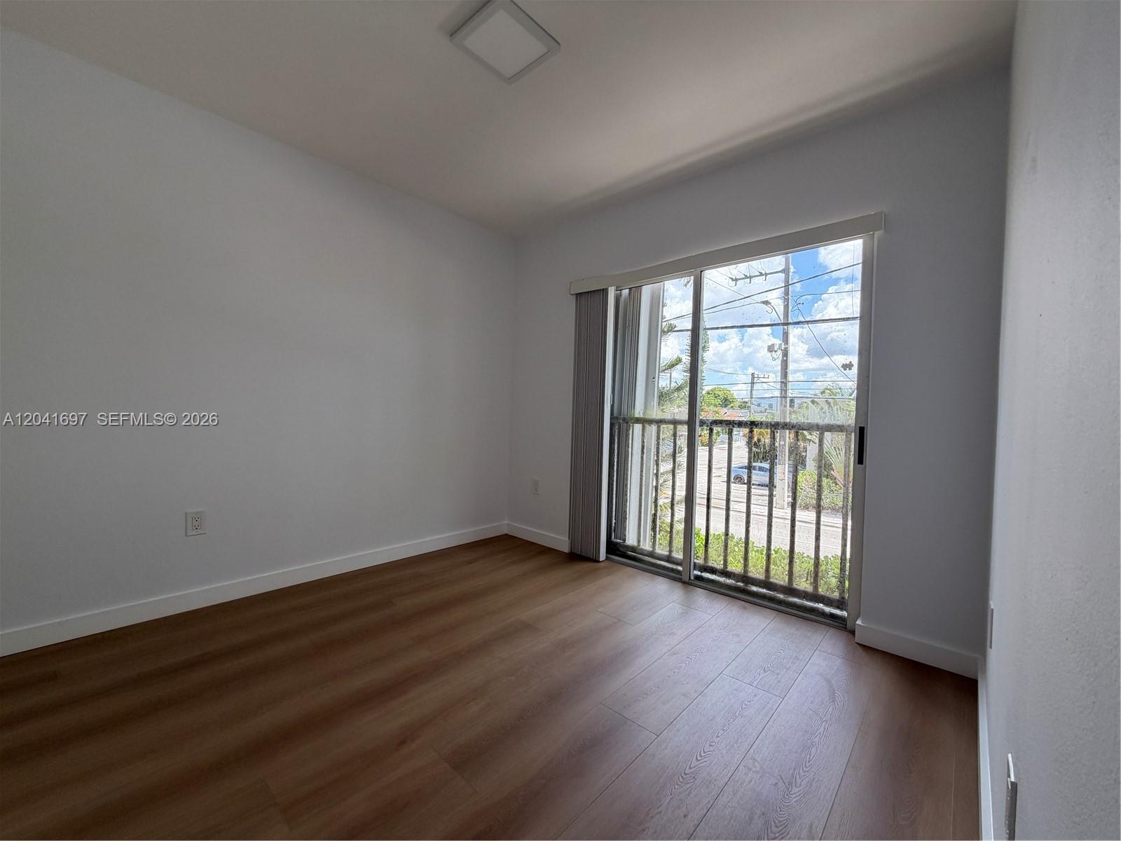An empty room with wood-look flooring, white walls, and a sliding glass door to a balcony — 717 SW 11th Ave # 206, Miami FL 33130, MIAMI, FL