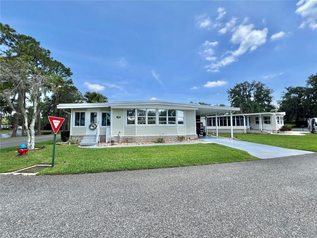A light-colored manufactured home features a carport, a front lawn, and a nearby fire hydrant — 105 TEMPLE COVE W, LEESBURG, FL