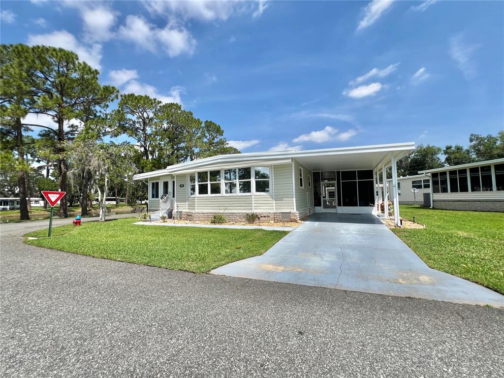 A grassy lawn borders a canal next to a road with mobile homes — 105 TEMPLE COVE W, LEESBURG, FL