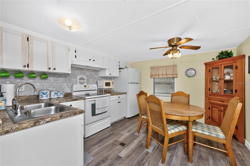 A kitchen features white cabinets, a faux-brick backsplash, a dining table, and wood-look flooring — 7459 DANVERS CIRCLE, PORT CHARLOTTE, FL