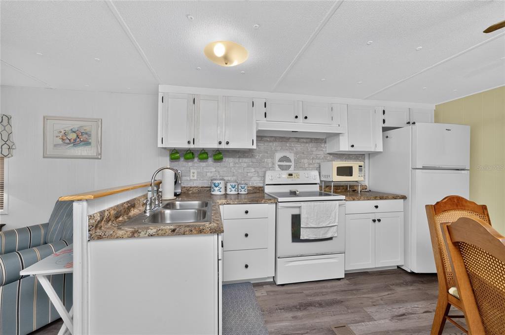 A kitchen features white cabinets, a faux-brick backsplash, laminate countertops, and a white stove — 7459 DANVERS CIRCLE, PORT CHARLOTTE, FL