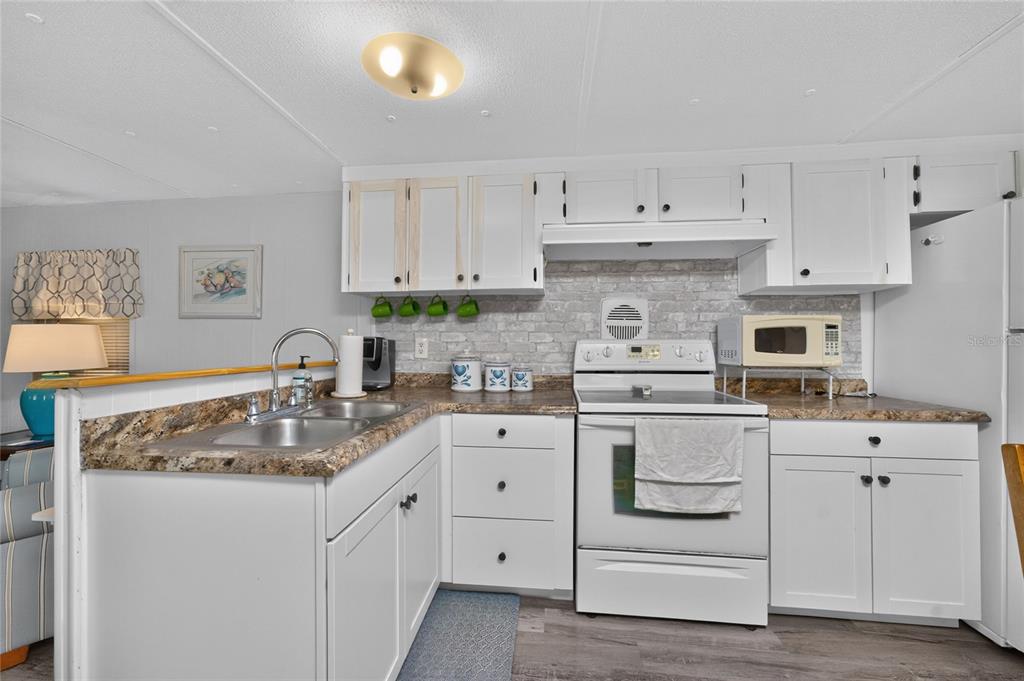 A kitchen features white cabinets, a faux brick backsplash, and a laminate countertop — 7459 DANVERS CIRCLE, PORT CHARLOTTE, FL