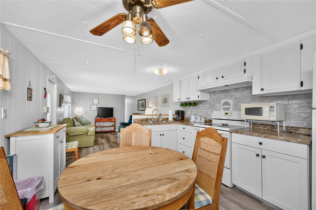 A kitchen and dining area with white cabinets, a round wooden table, and wood flooring — 7459 DANVERS CIRCLE, PORT CHARLOTTE, FL