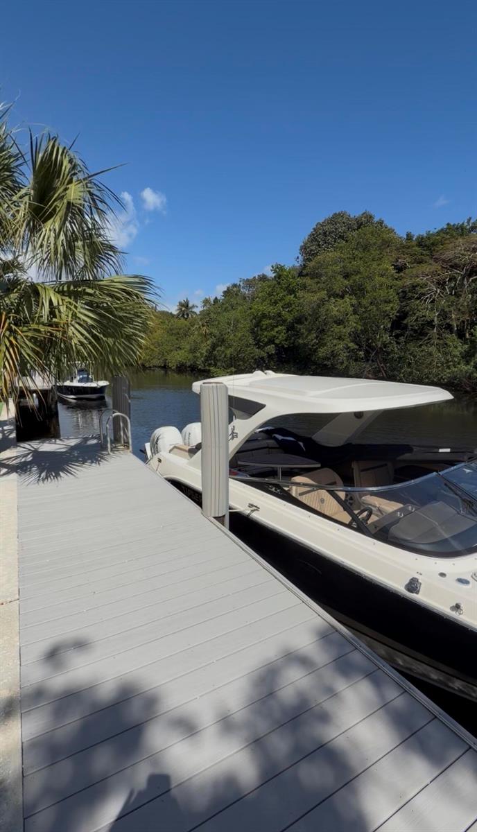 A white motorboat is docked at a gray wooden pier next to a lush canal — 550 SW 6th Avenue, Boca Raton FL 33486, BOCA RATON, FL