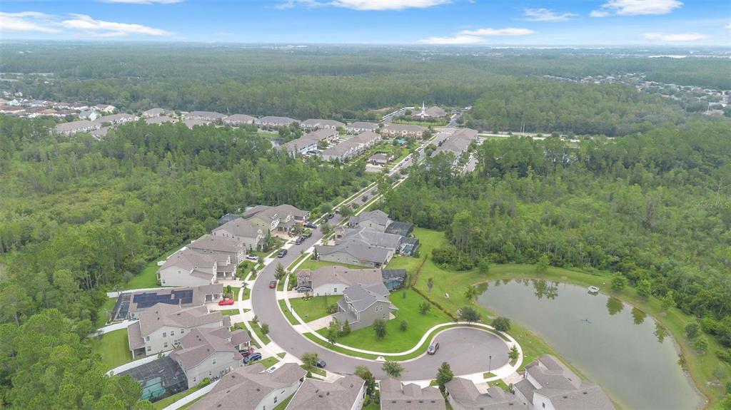 An aerial view shows a suburban neighborhood with houses surrounding a small pond and forest — 9247 LEGADO DRIVE, WINTER GARDEN, FL