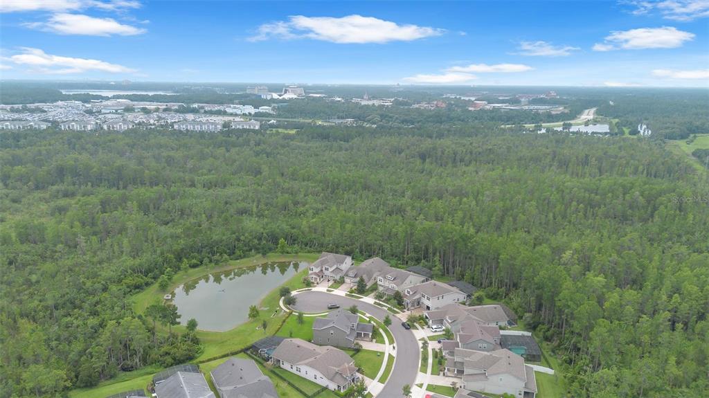 An aerial view shows a suburban neighborhood with houses, a pond, and surrounding forest — 9247 LEGADO DRIVE, WINTER GARDEN, FL