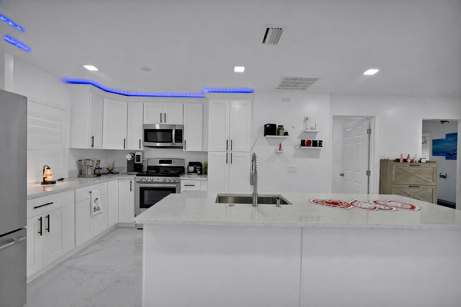 A modern white kitchen features a central island, stainless steel appliances, and blue accent lighting — 2404 Dade Road, Fort Pierce FL 34982, FORT PIERCE, FL