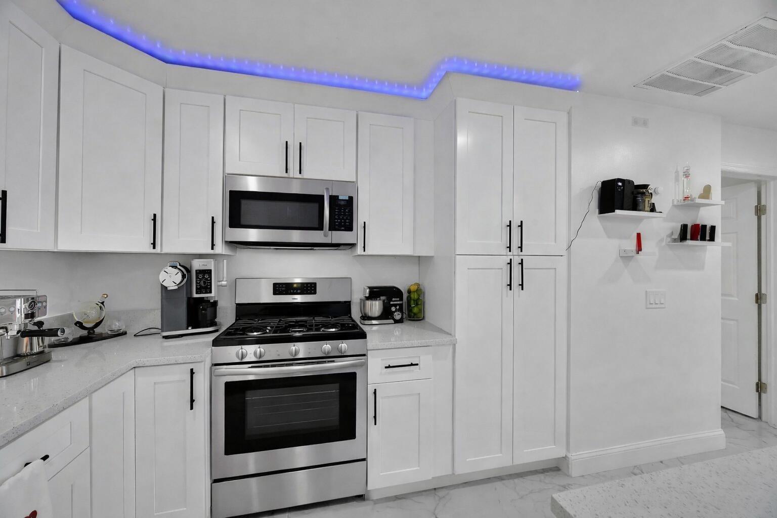 A modern kitchen features white cabinets, stainless steel appliances, and blue LED accent lighting — 2404 Dade Road, Fort Pierce FL 34982, FORT PIERCE, FL