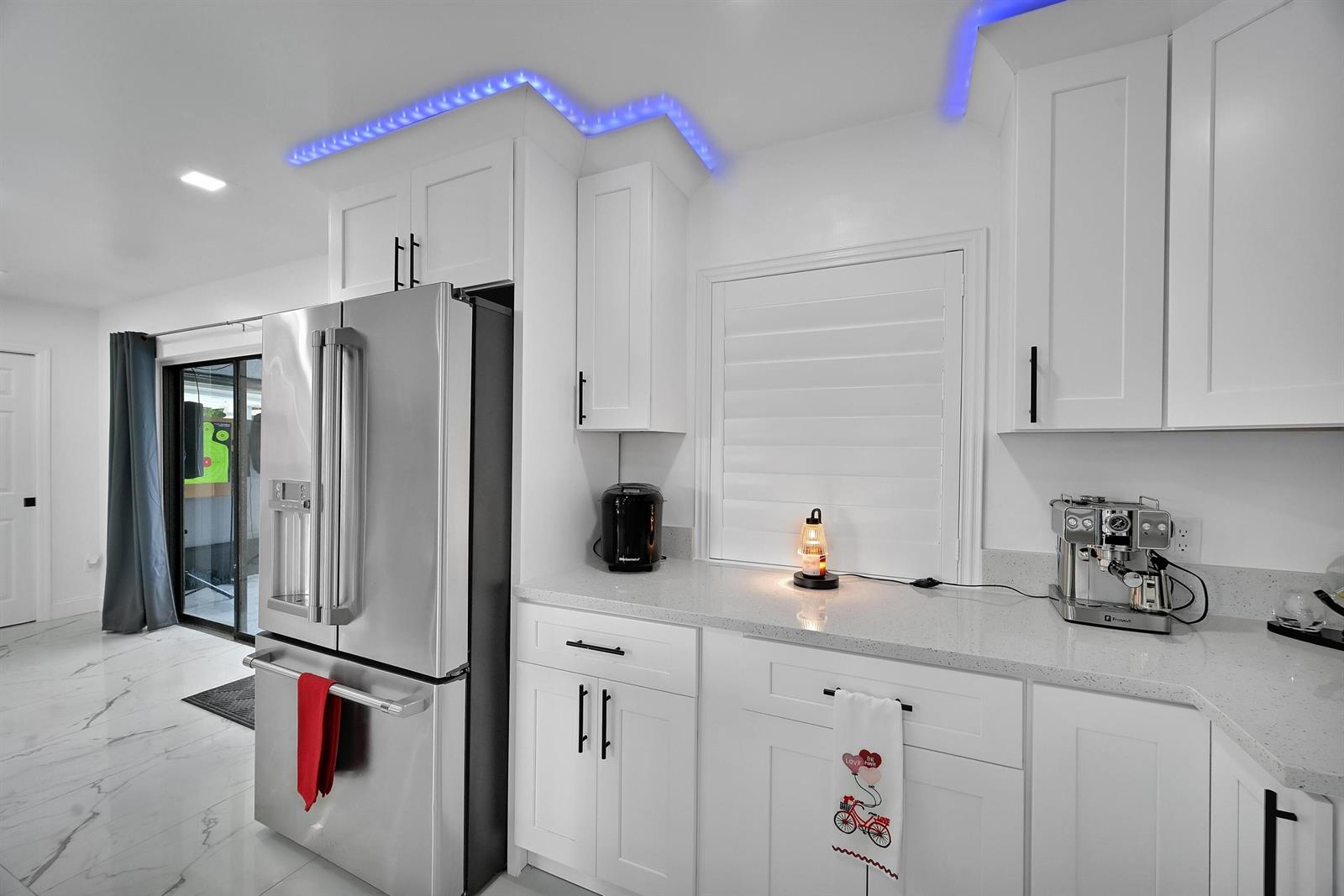 A modern kitchen features white cabinets, stainless steel appliances, quartz countertops, and blue LED lighting — 2404 Dade Road, Fort Pierce FL 34982, FORT PIERCE, FL