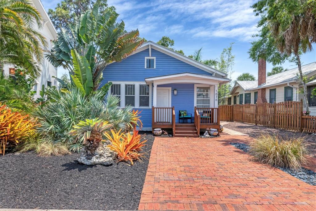 A blue house with a brick walkway and tropical landscaping sits under a blue sky — 1676 OAK STREET, SARASOTA, FL