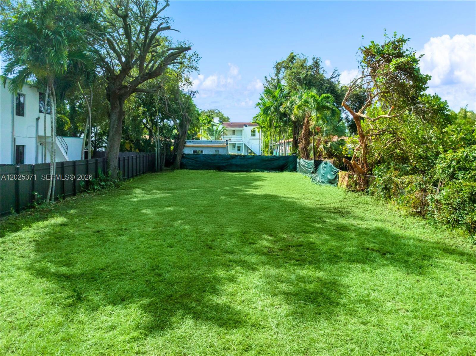 A large, grassy backyard is enclosed by a dark fence and surrounded by mature trees — 508 NE 67th St, Miami FL 33138, MIAMI, FL