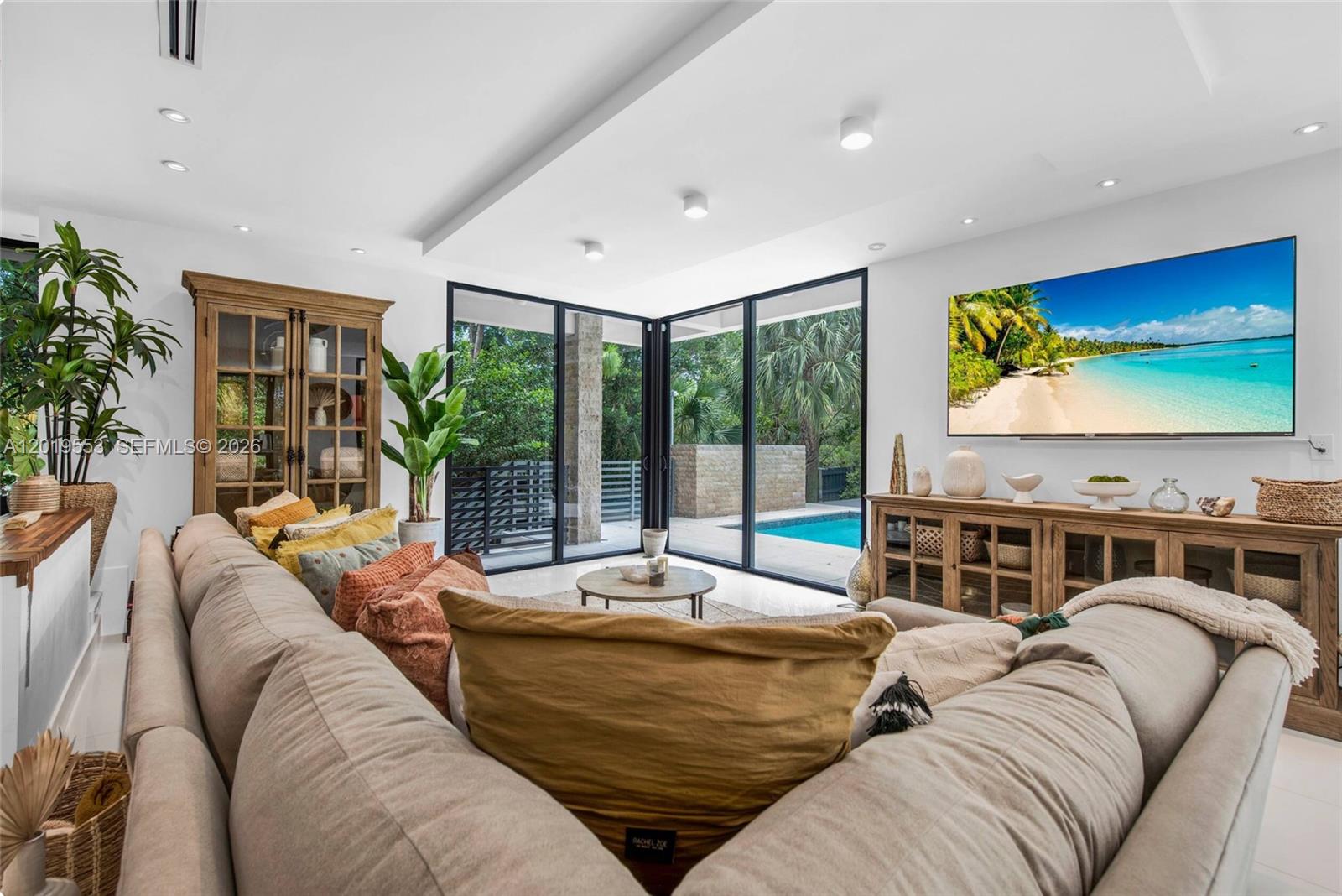 A living room features a large sectional sofa, a television, and floor-to-ceiling windows overlooking a pool — 994-990 NE 78th, Miami FL 33138, MIAMI, FL
