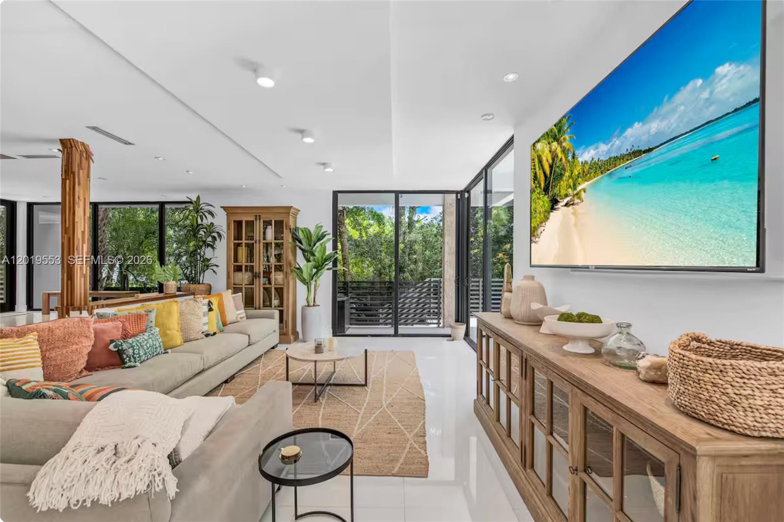 A bright living room features a large television, neutral sofa, and glass sliding doors — 994-990 NE 78th, Miami FL 33138, MIAMI, FL