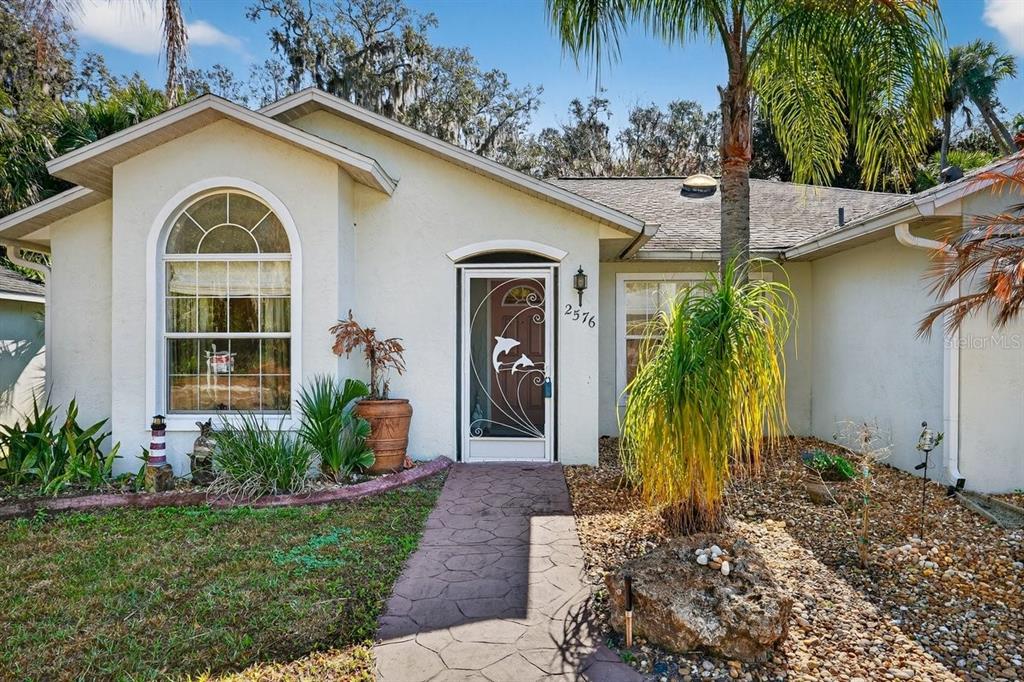 A single-story house with a white stucco exterior, arched window, and a dolphin-themed screen door — 2576 SHILO GLYNN LANE, NEW SMYRNA BEACH, FL