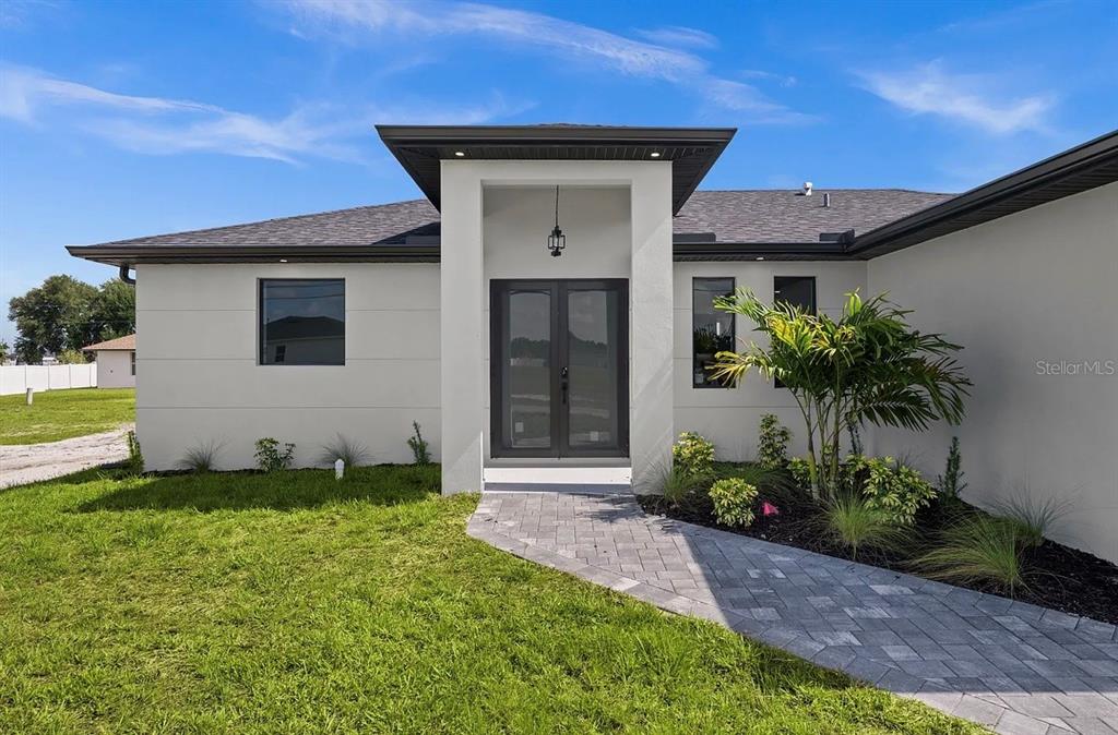 A modern house exterior features a white facade, a dark roof, and double glass doors — 1805 NW 12TH STREET, CAPE CORAL, FL
