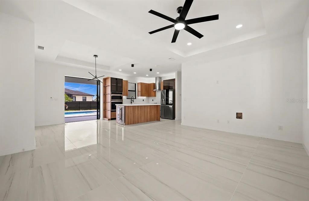 An open-concept living area with white tile floors, a modern kitchen, and a pool view — 1805 NW 12TH STREET, CAPE CORAL, FL