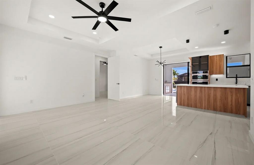 An open-concept living area features white tile floors, a ceiling fan, and a wood-accented kitchen — 1805 NW 12TH STREET, CAPE CORAL, FL