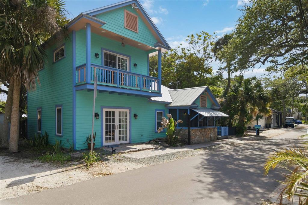A two-story turquoise house with a balcony and a stone-walled porch sits beside a road — 207 ESTHER STREET, NEW SMYRNA BEACH, FL