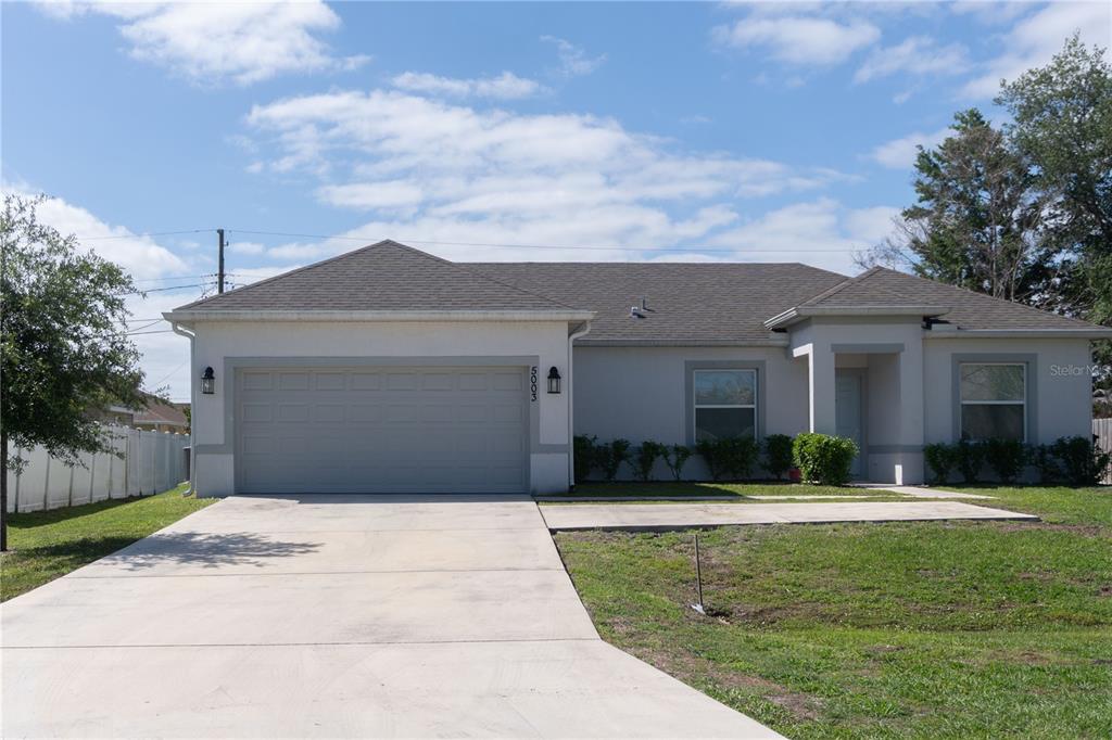 A single-story house with a gray garage door, light-colored stucco walls, and a concrete driveway — 5003 NW MANVILLE DRIVE, PORT ST LUCIE, FL