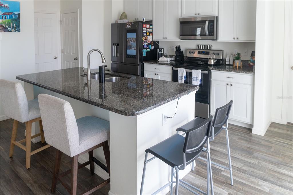 A kitchen features a granite-topped island, white cabinetry, stainless steel appliances, and four bar stools — 5003 NW MANVILLE DRIVE, PORT ST LUCIE, FL
