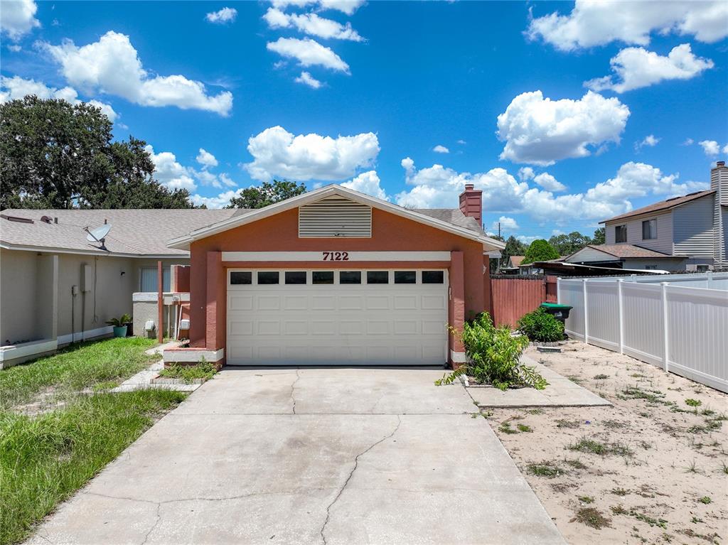 A single-story house exterior features a two-car garage, a concrete driveway, and a white fence — 7122 HARBOR HEIGHTS CIRCLE, ORLANDO, FL