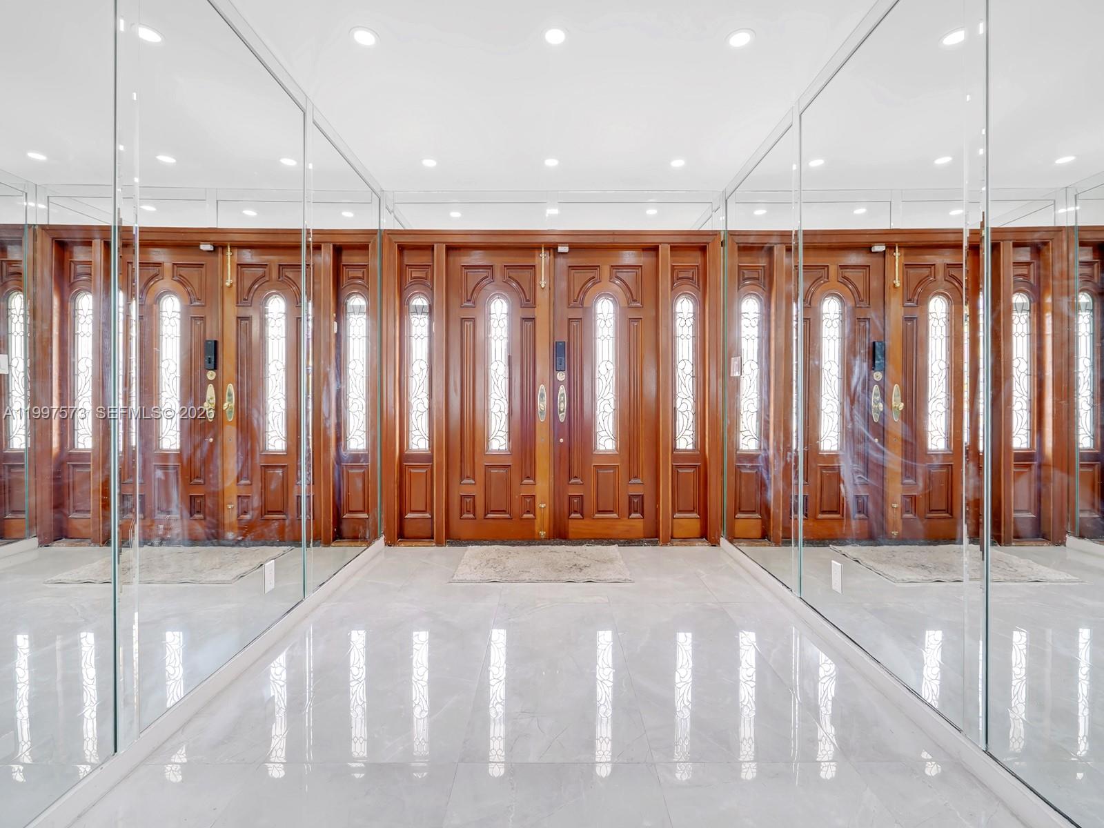 A foyer features double wooden doors flanked by floor-to-ceiling mirrors and light-colored tile flooring — 621 E Tropical Way, Plantation FL 33317, PLANTATION, FL