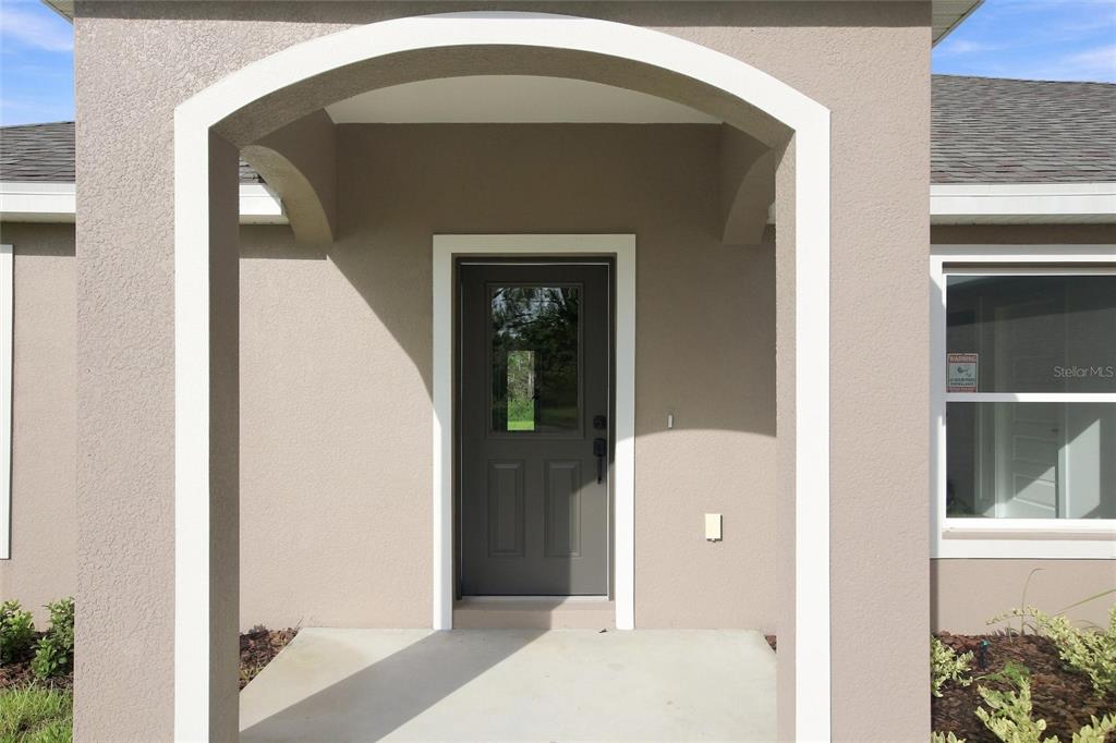 A covered entryway features a gray front door with a window under an arched portico — 6898 DICKINSON DRIVE, SEBRING, FL