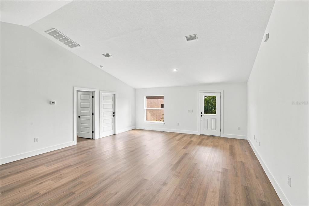 A spacious, empty room features white walls, vaulted ceilings, and light wood-look flooring — 6898 DICKINSON DRIVE, SEBRING, FL