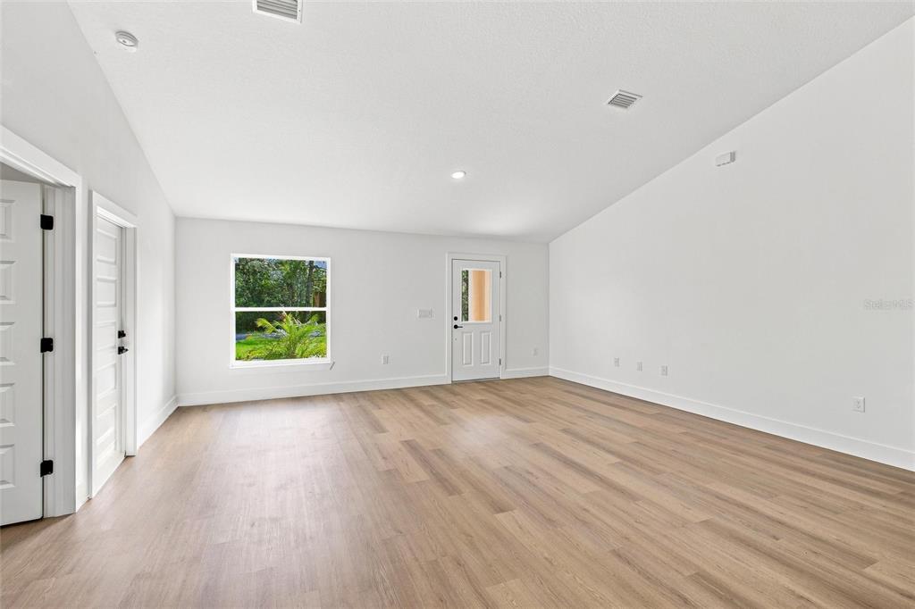 An empty room with white walls, light wood-look flooring, a window, and a glass-paneled door — 6898 DICKINSON DRIVE, SEBRING, FL