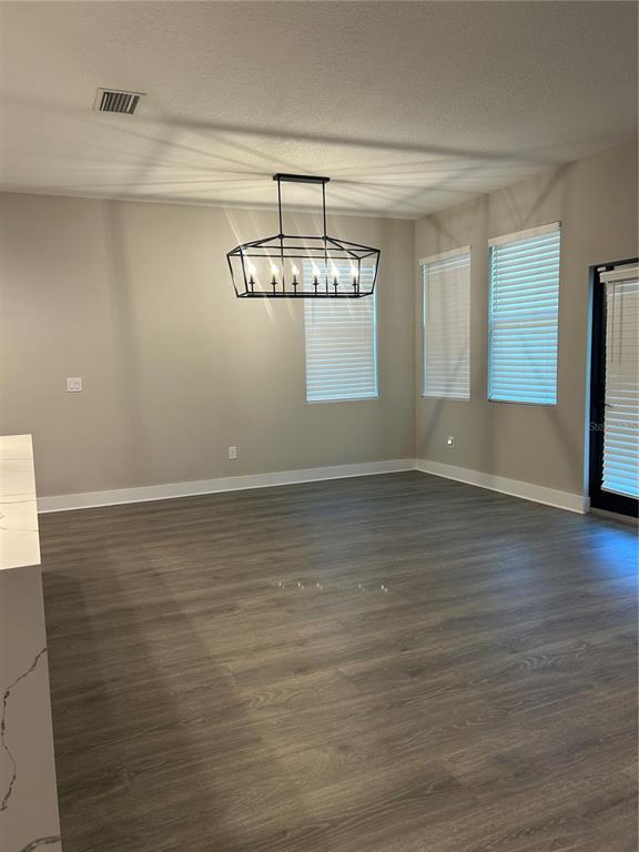 An empty dining area features wood-look flooring, a modern chandelier, and several windows with blinds — 2556 13TH AVENUE N, ST PETERSBURG, FL