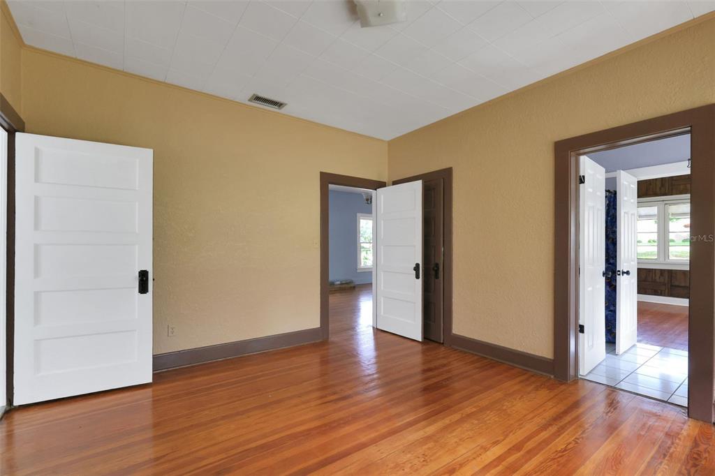 An interior view of a room with hardwood floors, tan walls, and three open doorways — 742 HIBISCUS AVENUE, LAKE WALES, FL