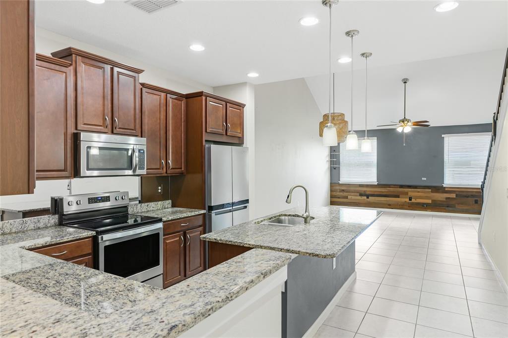 A kitchen with dark wood cabinets, granite countertops, and stainless steel appliances overlooks a living area — 3644 TIN CUP BOULEVARD, SARASOTA, FL