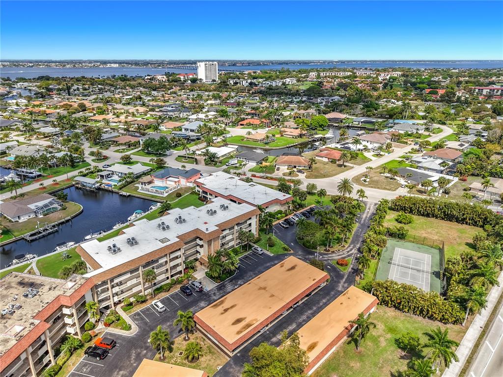 An aerial view shows a multi-story apartment complex with a tennis court and canal access — 4277 MARINER WAY UNIT 218, FORT MYERS, FL