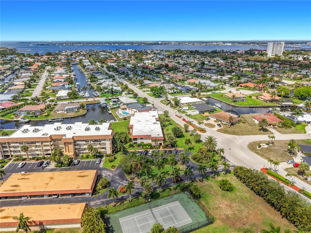 An aerial view shows residential buildings, a tennis court, and canals near a large body of water — 4277 MARINER WAY UNIT 218, FORT MYERS, FL