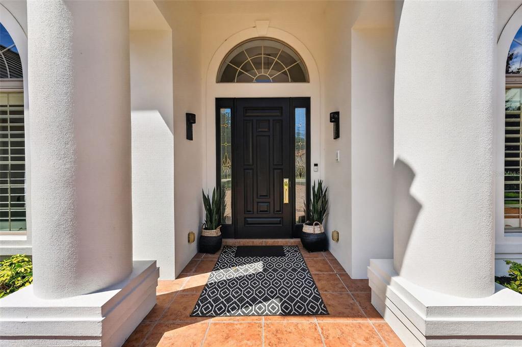 A dark front door with sidelights and an arched transom sits between two white columns — 9616 SAN FERNANDO COURT, HOWEY IN THE HILLS, FL