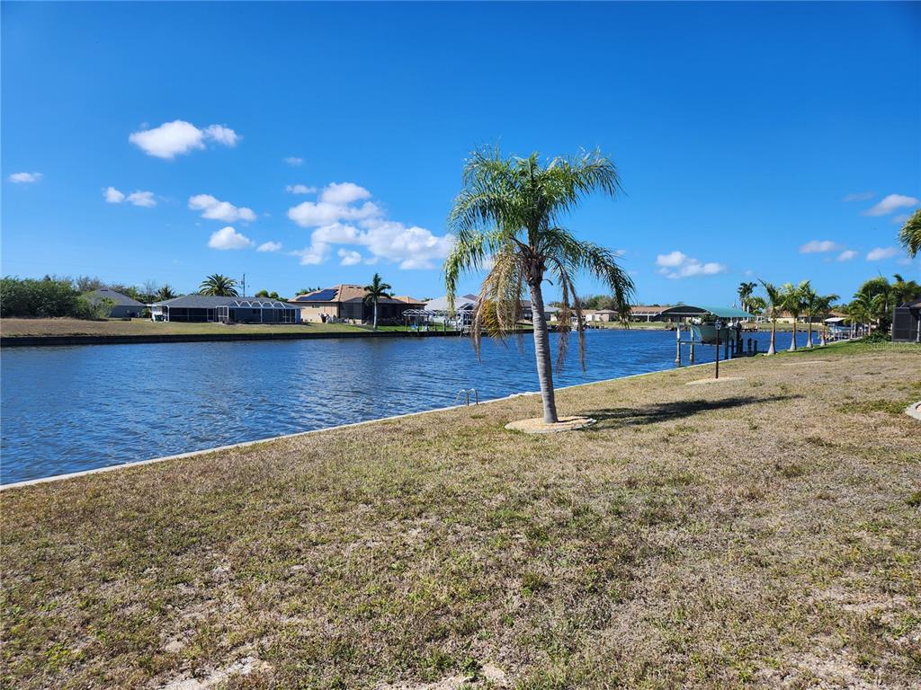 A palm tree stands on a grassy lawn overlooking a canal with houses in the distance — 15332 ALSASK CIRCLE, PORT CHARLOTTE, FL