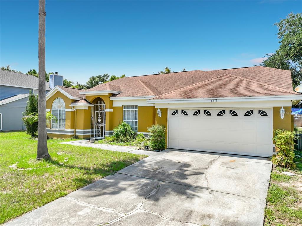 A single-story house with a yellow stucco exterior, brown roof, and a two-car garage — 5579 RED BONE LANE, ORLANDO, FL