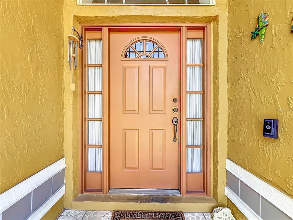 A front entrance with a peach-colored door, sidelights, and yellow stucco exterior walls — 5579 RED BONE LANE, ORLANDO, FL