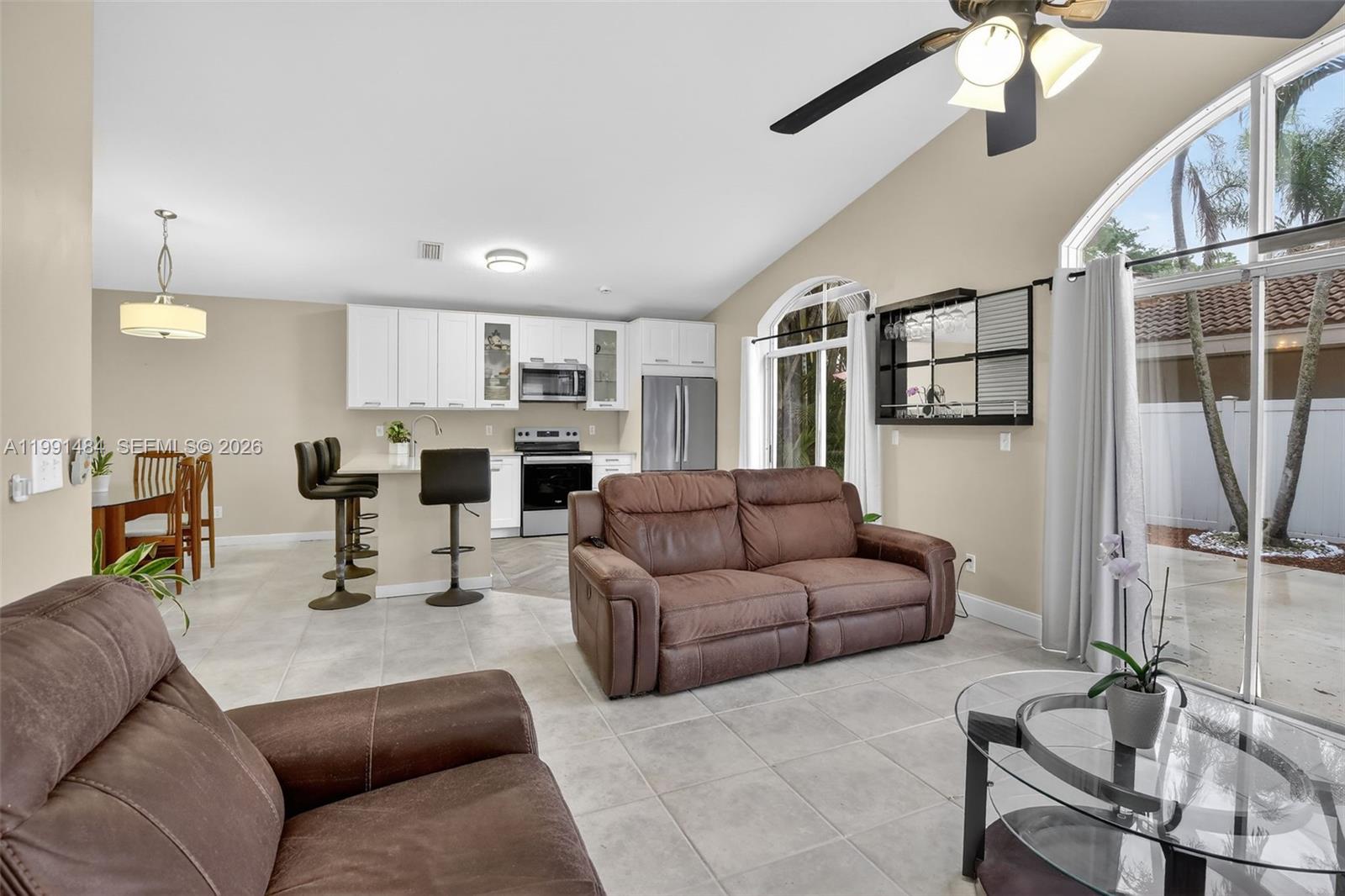 An open-concept living room and kitchen featuring brown leather furniture, white cabinetry, and tile flooring — 922 Opal Ter, Weston FL 33326, WESTON, FL