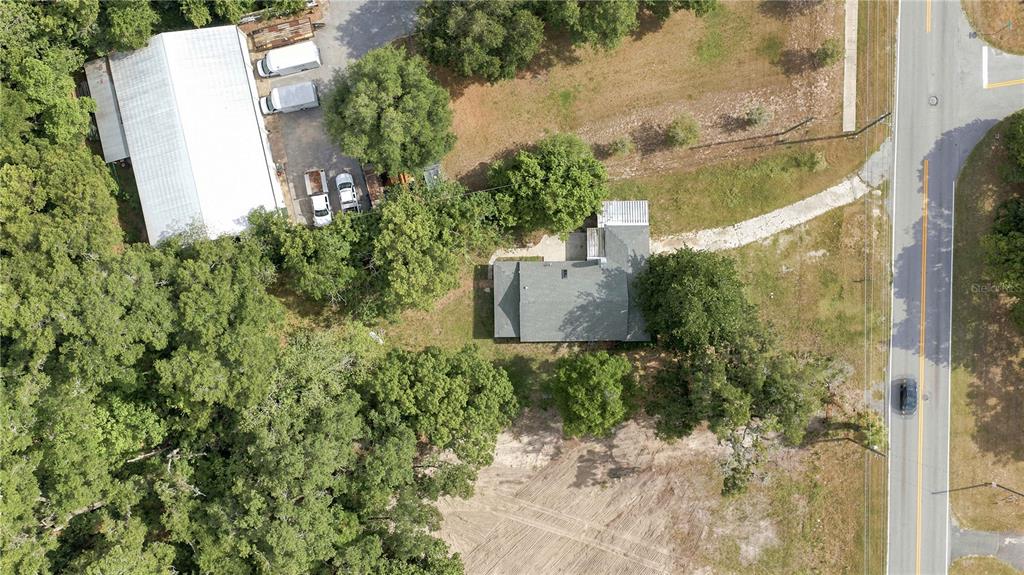 An aerial view shows a house, a large metal workshop, and vehicles on a wooded lot — 2107 NE 8TH ROAD, OCALA, FL