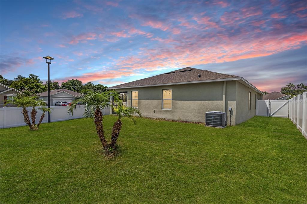 A grassy backyard features two small palm trees, a white vinyl fence, and a house exterior — 1097 AUGUST SKY DRIVE, DELTONA, FL