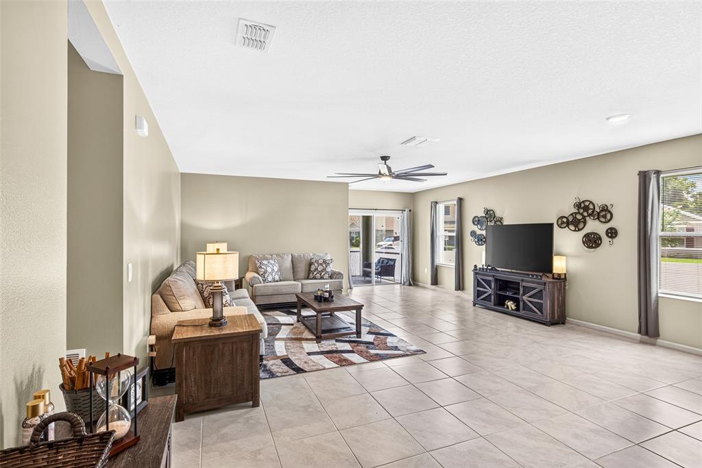 A spacious living room features tile flooring, a ceiling fan, and a sliding glass door — 1097 AUGUST SKY DRIVE, DELTONA, FL