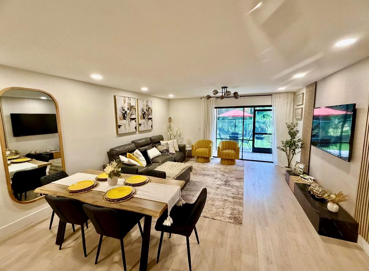 An open-concept living and dining area features a dark sofa, yellow armchairs, and wood flooring — 22415 SW 61st Way # 106, Boca Raton FL 33428, BOCA RATON, FL